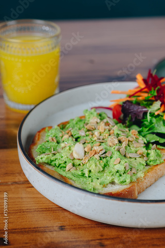 A plate of avocado toast with a side of vegetables and a glass of orange juice