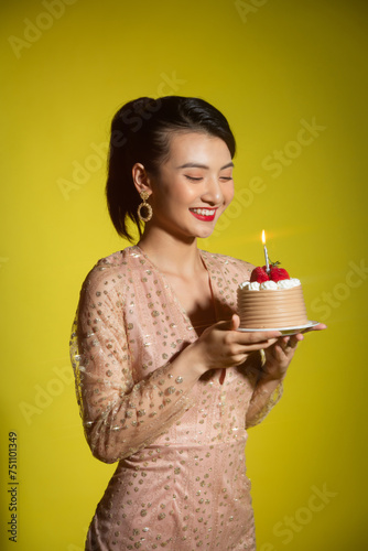 Pretty young asian female looking at burning candle on birthday photo