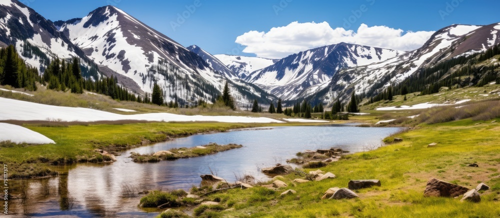 A view of a majestic mountain range with snow-capped peaks towering in the background, while a river flows in the foreground. The scene showcases the rugged beauty of nature with the contrast between