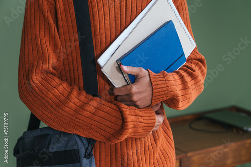 Young man holding student stuff over green wall