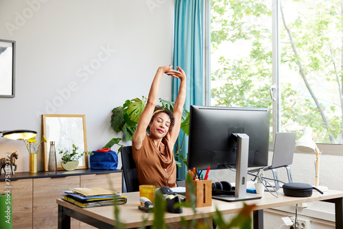Tired woman stretching arms at computer desk in office
