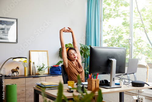 Tired freelancer with raised arms at desk in office photo