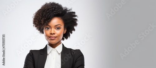A young African woman with black hair confidently poses in a professional suit and tie, with her arms crossed. She exudes leadership and assertiveness in a business setting, against an isolated white photo