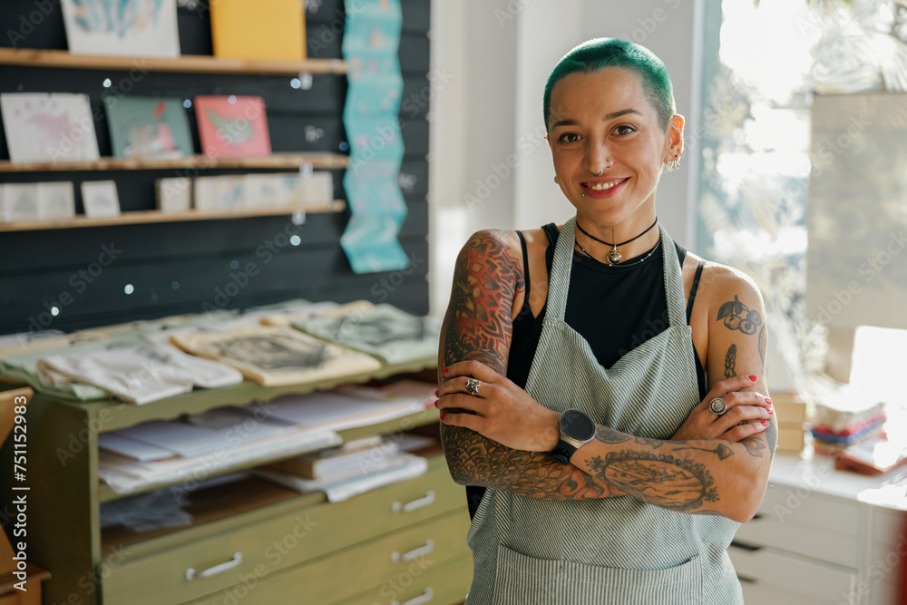 Smiling female designer standing with crossed hands on background of workshop and looks camera Smiling female designer standing with crossed hands on background of workshop and looks camera