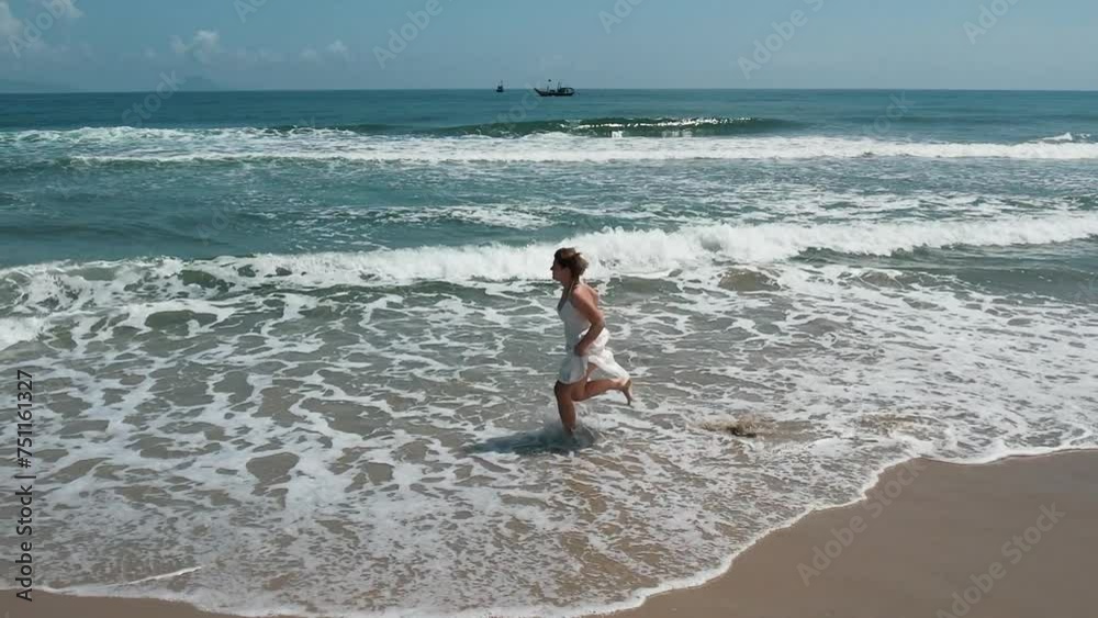 Young adult woman in a white dress joyfully running along a sandy beach shoreline, with gentle waves and distant boats on a sunny day, conveying freedom and Earth Days connection to nature Young adult woman in a white dress joyfully running along a sandy beach shoreline, with gentle waves and distant boats on a sunny day, conveying freedom and Earth Days connection to nature