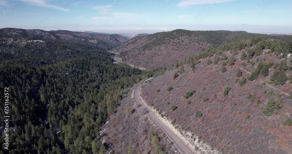A car drives along a mountain highway with forest below, drone aerial