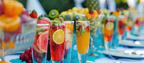 A table is covered with glasses filled with various types of fresh fruit juices  each garnished with colorful fruit pieces. The array of drinks presents a vibrant and refreshing display.
