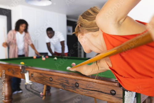 Young Caucasian woman plays pool, focusing intently on her shot