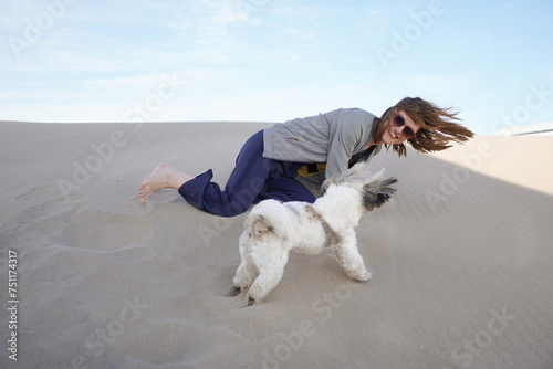 A woman playing with a shih tzu dog in the sand photo