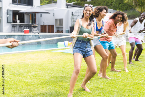 Diverse group of friends enjoy a tug-of-war game on a sunny lawn with copy space