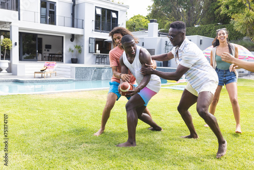 фотографія Diverse group of friends playfully tussle over a ball in a sunny backyard with c