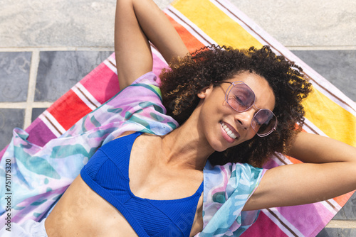 A biracial woman enjoys the sun while lying on a colorful towel