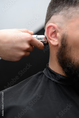 Barber shaves the temple with cordless trimmer during a short haircut on the sides of the head.