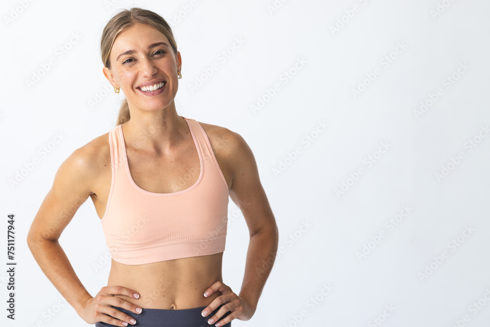 Young Caucasian woman smiles confidently, hands on hips, with copy space
