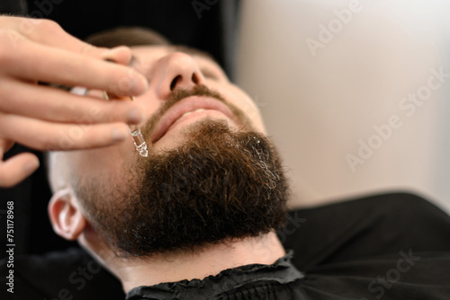 A barber stylist applies drops of oil to the client beard to moisturize and soften.