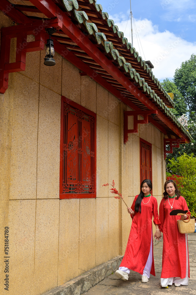 Happy Vietnamese mother and daughter in red ao dai dress in the park outdoor