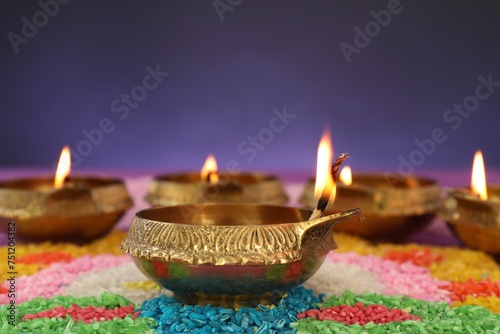 Diwali celebration. Diya lamps and colorful rangoli against purple background, closeup