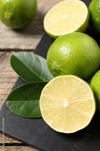 Fresh limes and green leaves on wooden table, closeup