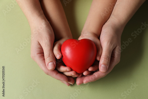 Mother and her child holding red decorative heart on light green background  top view