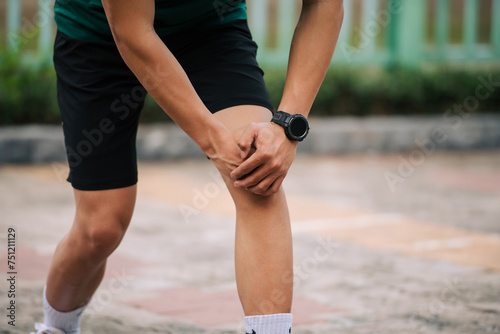 The asian man use hands hold on his knee while running on road photo