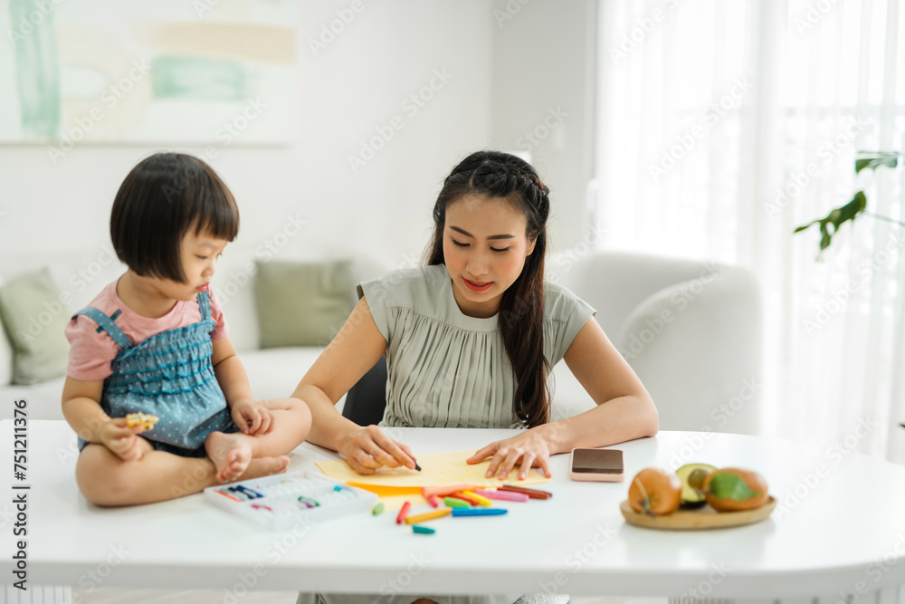 Freelancer mother assisting daughter drawing in notebook at table Freelancer mother assisting daughter drawing in notebook at table