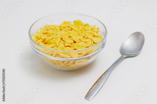 Corn flakes served in glass bowl with spoon on white