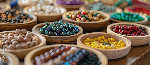 Handmade wooden bowls are filled with assorted beads - wooden, felt, ceramic, and glass - displayed on a table. The image features a shallow focus on the beads.