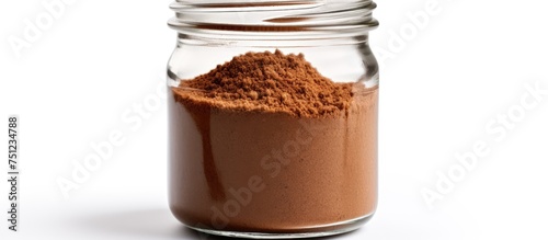 A glass jar filled with brown powder, most likely instant coffee, is placed on top of a clean white table. The jar is the focal point of the image, standing out against the bright background.