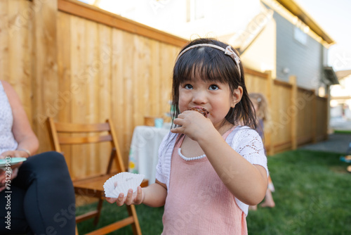 Girl in pink dress enjoying eating brownie with her hands.