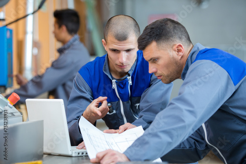 two men working with laptop in factory