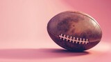 old leather football sits against a pink backdrop