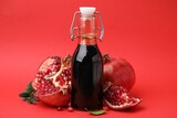 Tasty pomegranate sauce in bottle and fruits on red background, closeup