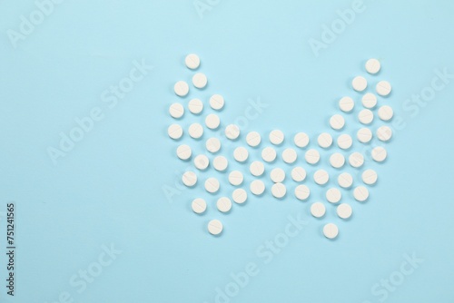 Endocrinology, Shape of thyroid gland made of pills on light blue background, flat lay. Space for text