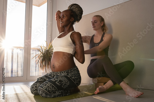 Black pregnant lady doing Sukha Gomukhasana with coach photo