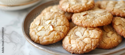 A plate on a wooden table is filled with freshly baked almond cookies, offering a tempting treat to anyone nearby. The cookies are golden brown and beautifully textured, hinting at a delicious