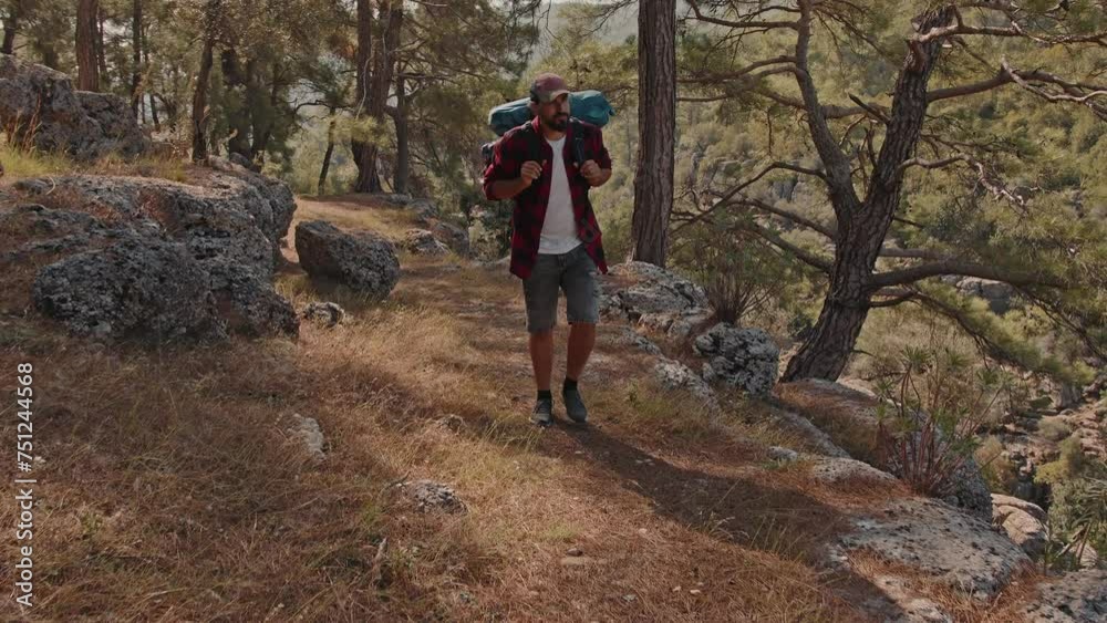 A tourist with a hiking backpack walks along a rocky path in a coniferous forest A tourist with a hiking backpack walks along a rocky path in a coniferous forest