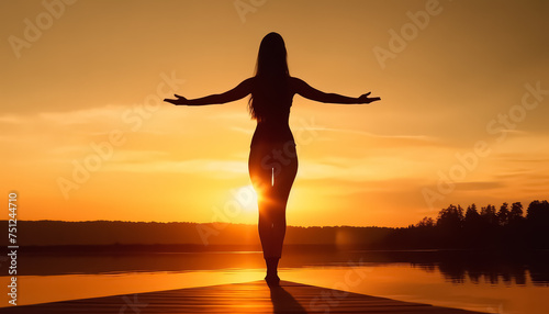 A woman is standing on a rock by the ocean  with her arms outstretched