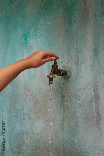 Hand opening a water tap and mint green wall woith texture photo