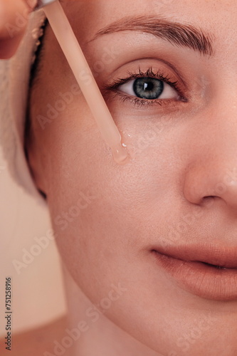 A young girl applies serum to her face.