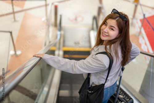 An attractive, positive Asian female tourist is on an escalator in the airport, traveling by plane.