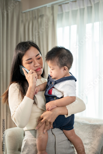 An unhappy Asian mom is calling her husband to come home to help her take care of their baby boy.