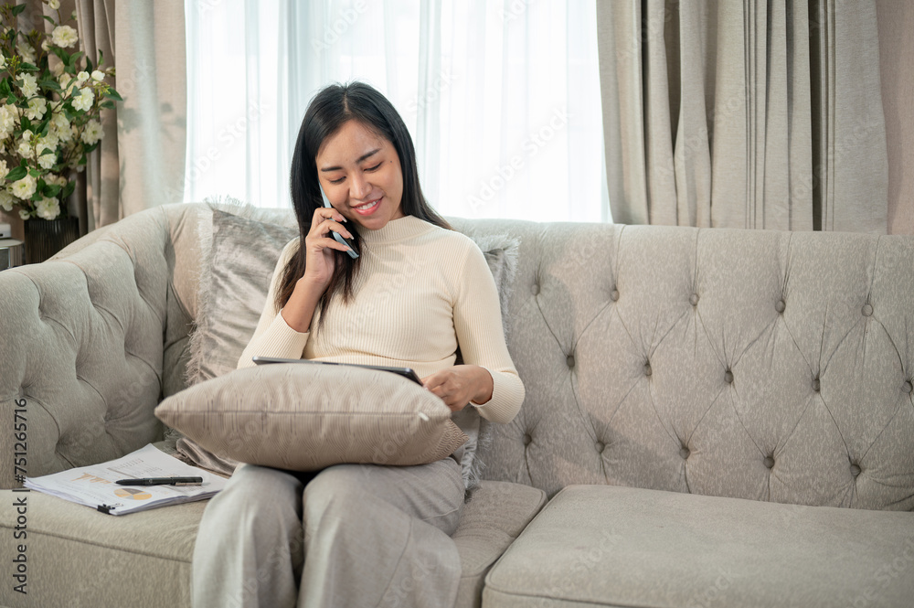 A businesswoman is multitasking, talking on the phone, and focusing on her tablet, working from home A businesswoman is multitasking, talking on the phone, and focusing on her tablet, working from home