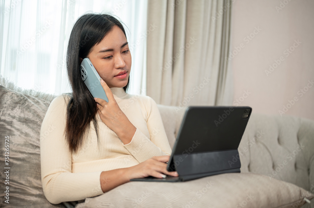 A businesswoman is multitasking, talking on the phone, and focusing on her tablet, working from home A businesswoman is multitasking, talking on the phone, and focusing on her tablet, working from home