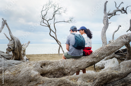 Couple sitting on the fallen tree trunk by the beach. Long Bay coastal Okura Track. Auckland. photo