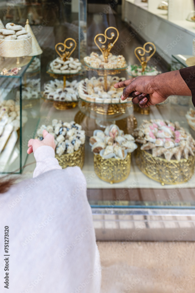 Vertical photo selecting Arabic sweets at a pastry shop. Food and culture concept.