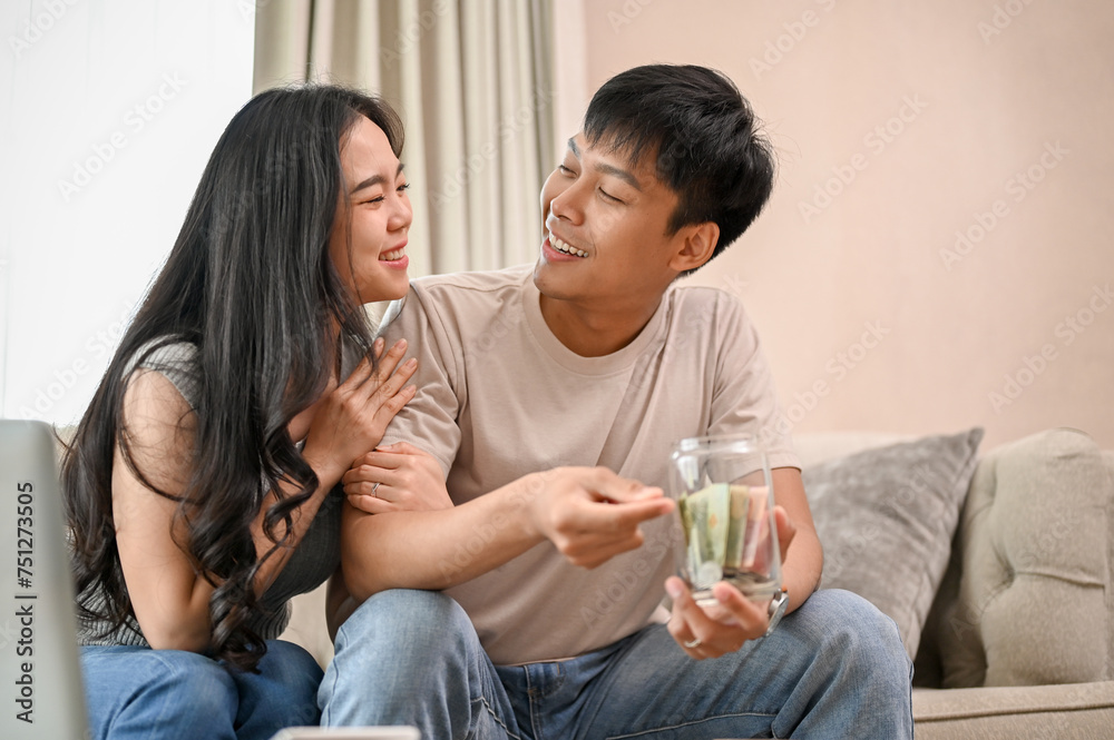 A lovely, happy young Asian new married couple is planning their savings together in the living room A lovely, happy young Asian new married couple is planning their savings together in the living room