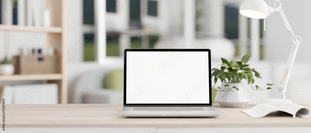 A white-screen laptop computer mockup on a wooden desk in a modern bright living room. - obrazy, fototapety, plakaty 