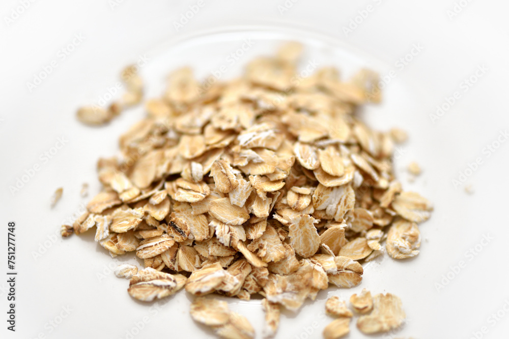Dry rolled oat flakes oatmeal on white plate Dry rolled oat flakes oatmeal on white plate