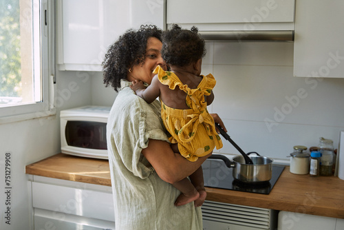 Grandmother holding her granddaughter while cooking in the kitchen photo