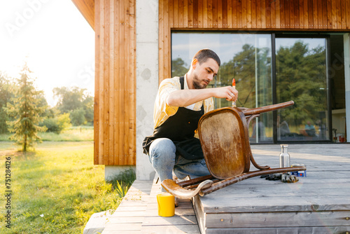 A man varnishes a chair outdoors photo